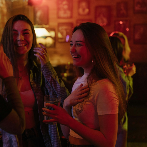 Two women smiling and chatting at a networking event in a casual, warm-lit environment.