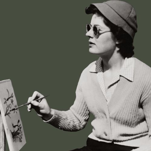 A vintage black-and-white photo of an artist wearing a hat and sunglasses, painting on a small canvas outdoors. The artist holds a paintbrush in hand, focused on creating nature-inspired artwork.