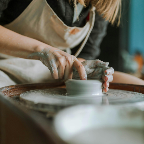 A person working with clay on a pottery wheel, shaping a small ceramic piece with their hands. The image shows detailed focus on the artist's hands covered in clay, demonstrating a creative process.Etsy vs Shopify