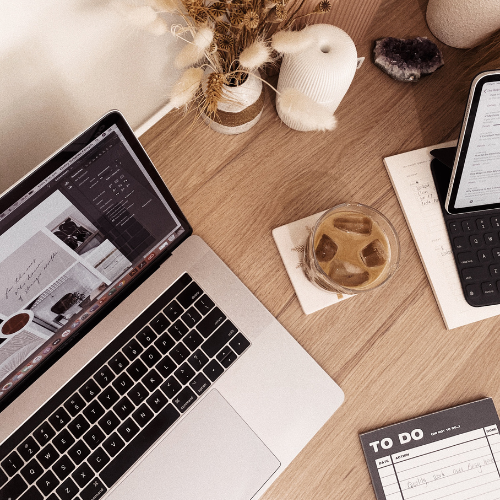 Workspace of a Toronto web designer featuring a laptop with a web design project, iced coffee, and a notepad on a wooden desk, discussing Black Friday small business strategies.