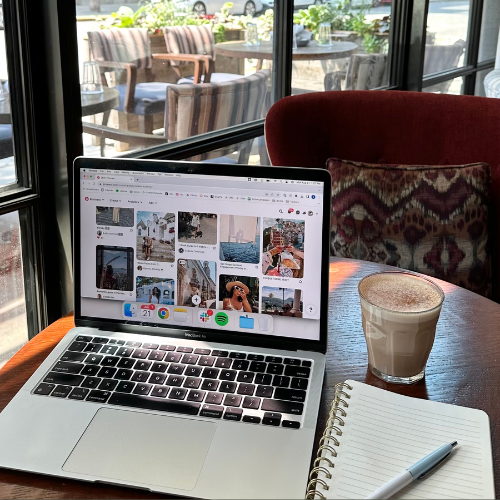 Open laptop on a café table showing Pinterest with a notebook and coffee beside it, representing ways to use Pinterest to drive traffic to a website.