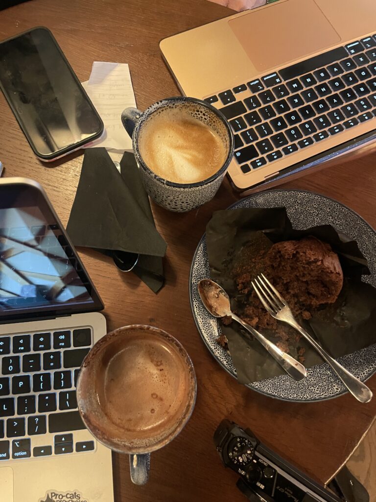 A cozy workspace with two laptops, a smartphone, mugs of coffee, and a partially eaten chocolate muffin, symbolizing productivity and focus on homepage SEO optimization.