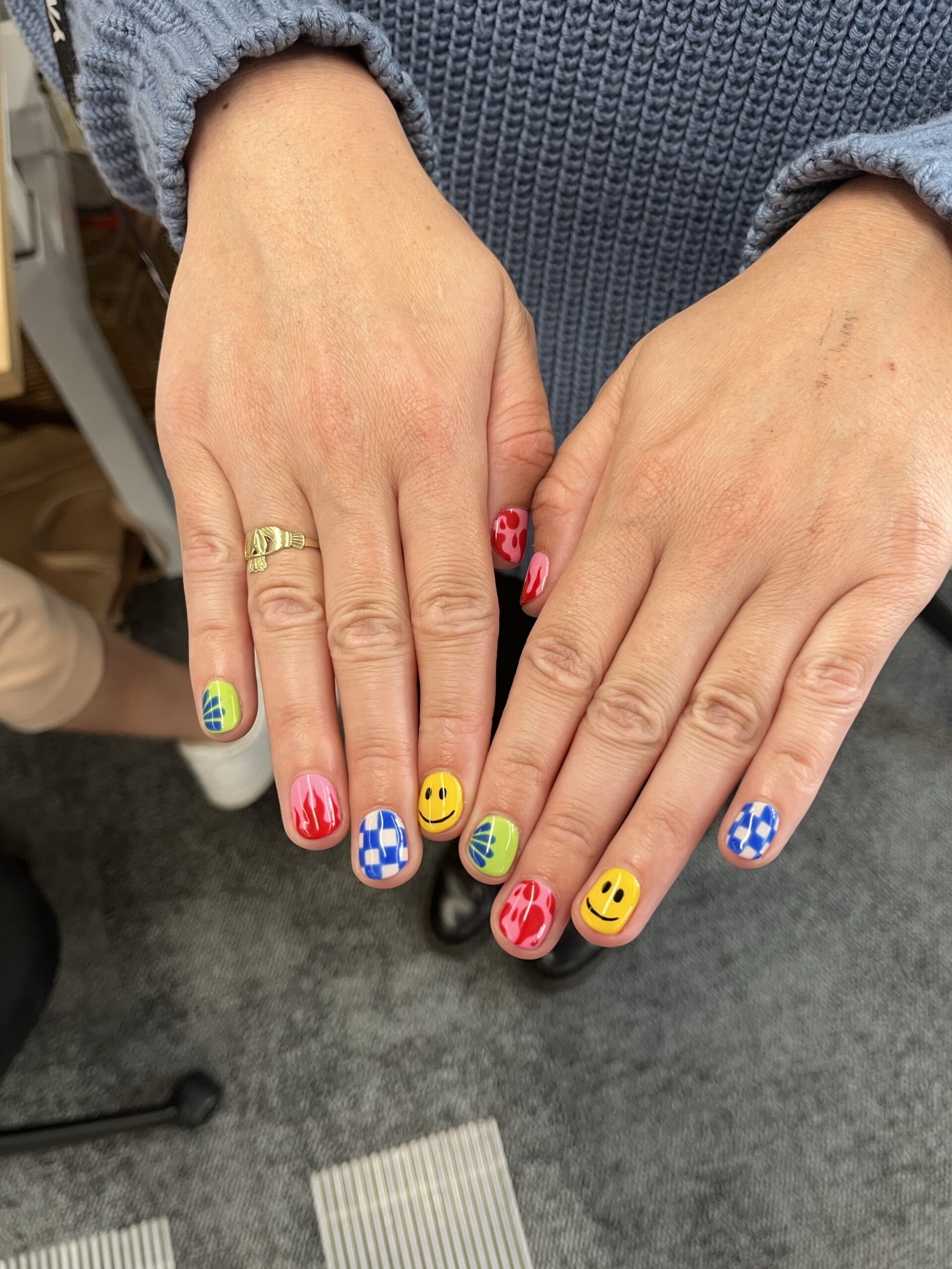 Close-up of two hands with brightly colored, mismatched nail art featuring smiley faces, flames, and checkerboard patterns, symbolizing a creative, authentic style that stands out from competitors.
